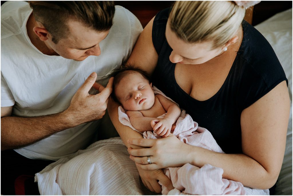 New parents holding sleeping baby girl during newborn lifestyle session.
