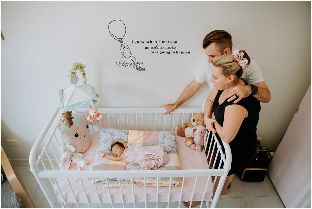 Husband and wife watching newborn daughter in crib during newborn lifestyle photo shoot.