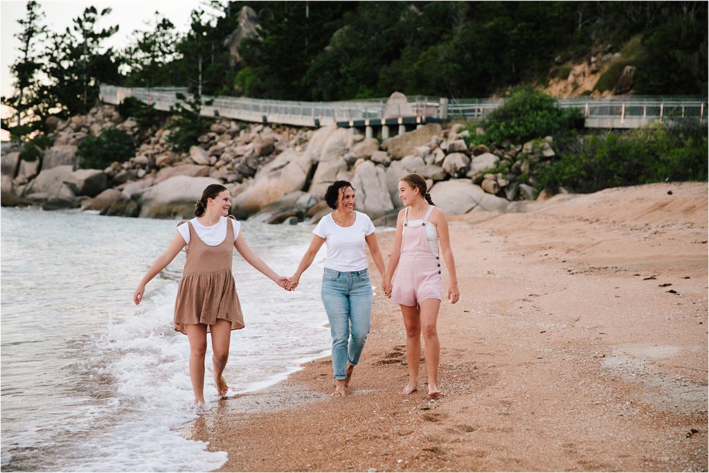 Mother and two older daughters holding hands walking down beach.