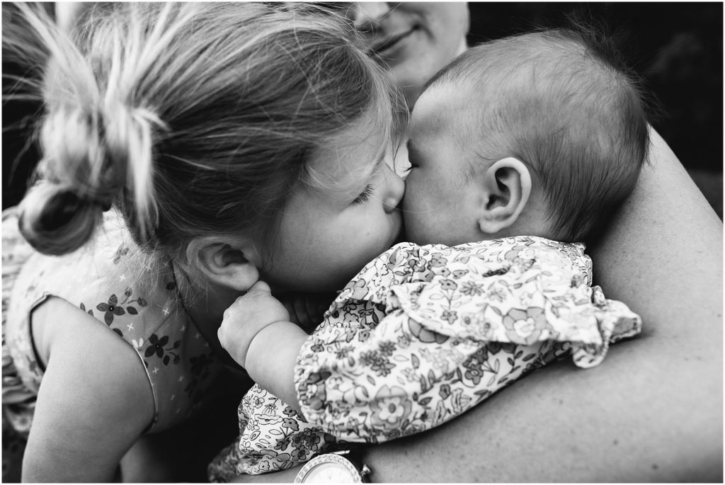 Older sister kissing baby sister on cheek.