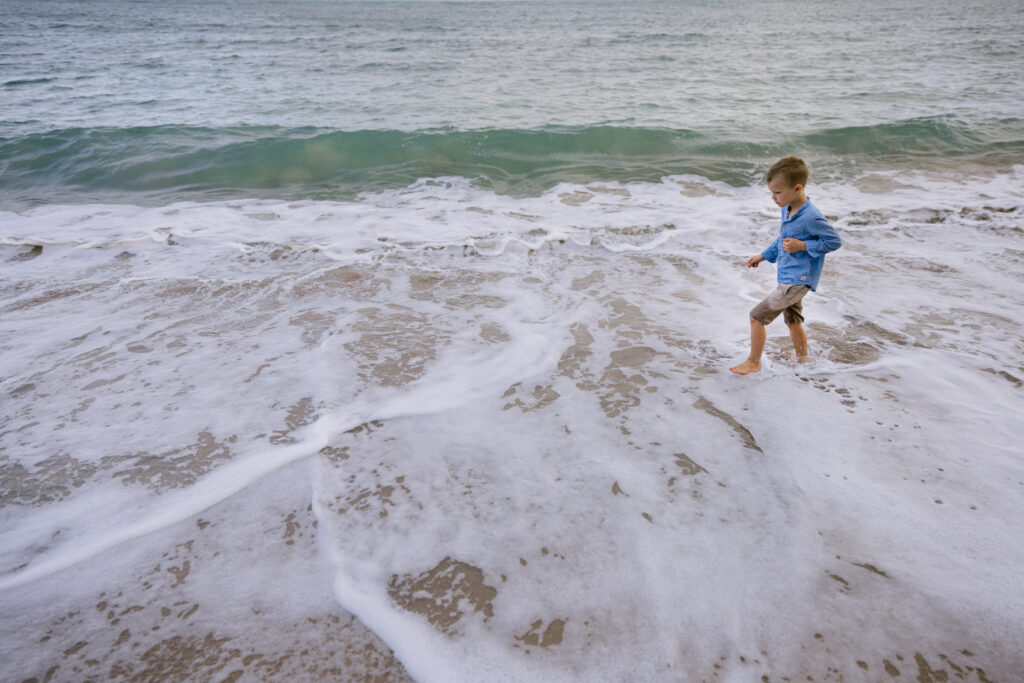 The young boy walks in the shallow water as the waves roll in at Geoffrey Bay Magnetic Island.