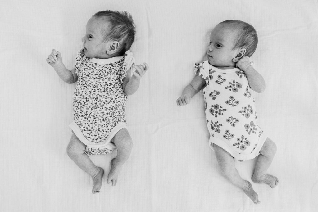 Twin girls four weeks old lying in their cot next to each other.