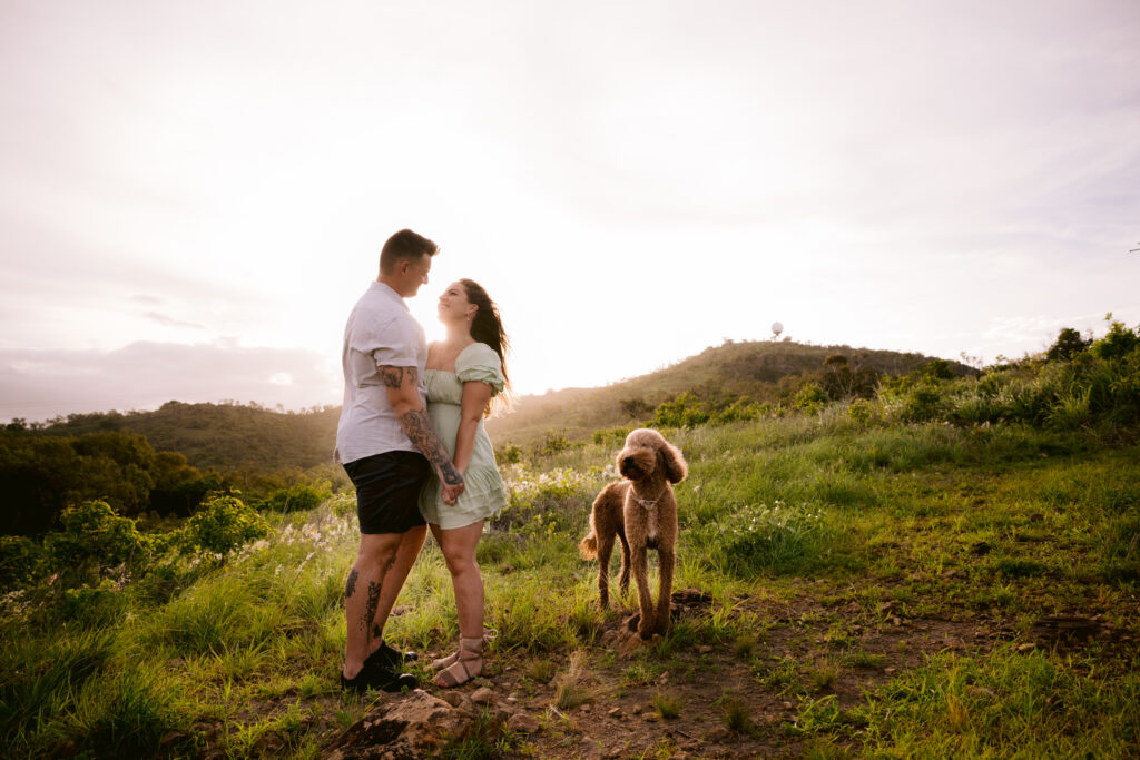 The couple look lovingly at each other as their dog Mopsy stands near them on the green grassy hill in Townsville.