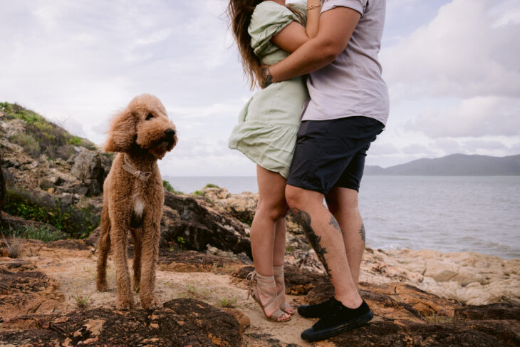 Trudy and Beau's engagement photo. Trudy is on tiptoes kissing Beau and Mopsy the groodle is standing beside.