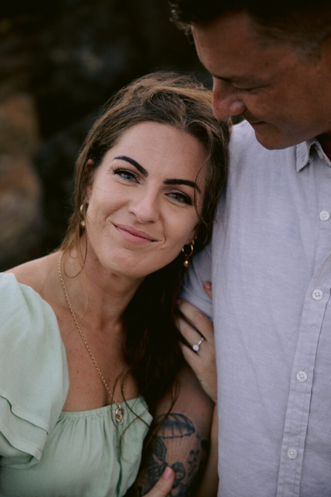 an engagement photo of Trudy with her hands wrapped around her Fiancé Beau's arm and her engagement ring is visible. Beau looks down at Trudy lovingly.