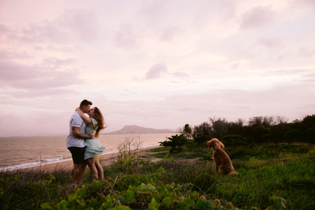 Engagement photo of Trudy and Beau with their dog at sunset on a hill near the beach.