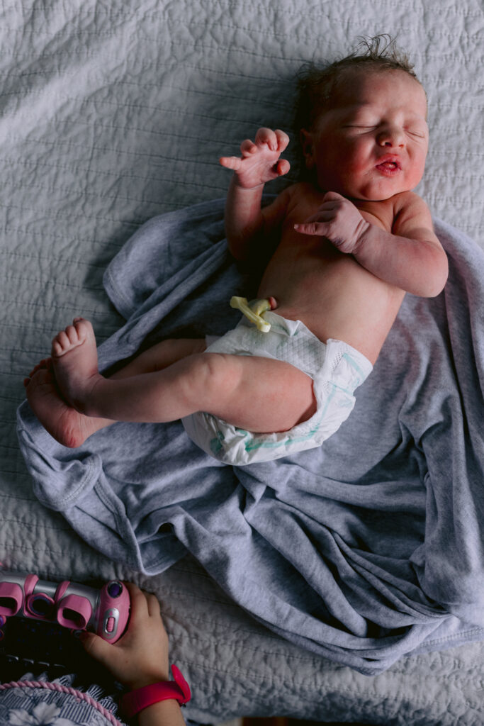 Newborn baby boy laying in a nappy. Big sister stands near with a camera in her hands