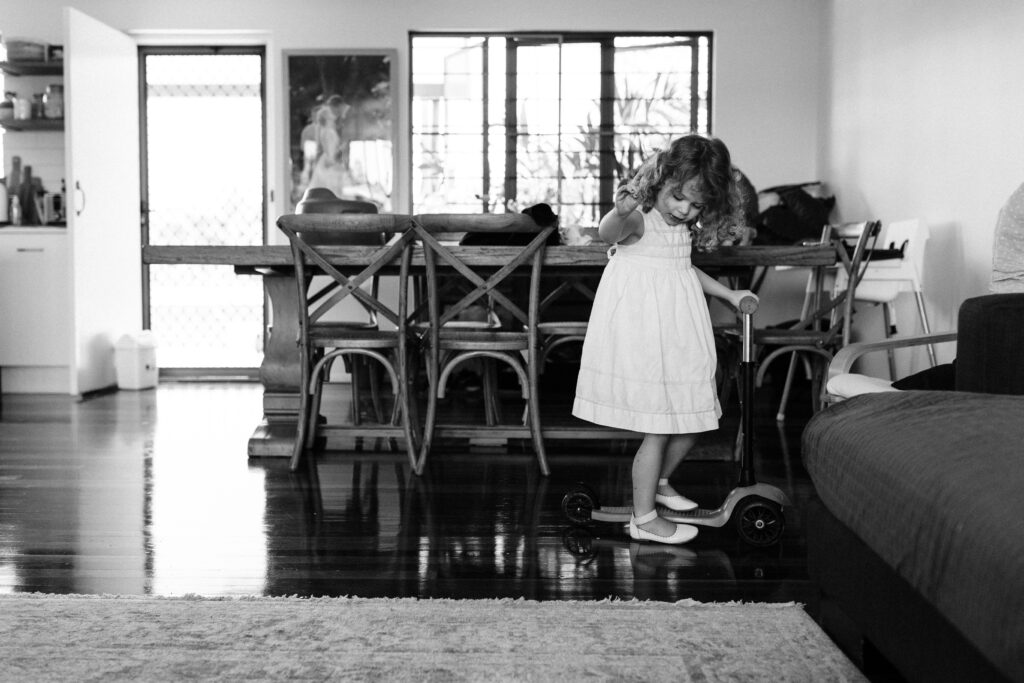Pip stands on her scooter near the dining room table. She is wearing a white dress and white shoes.