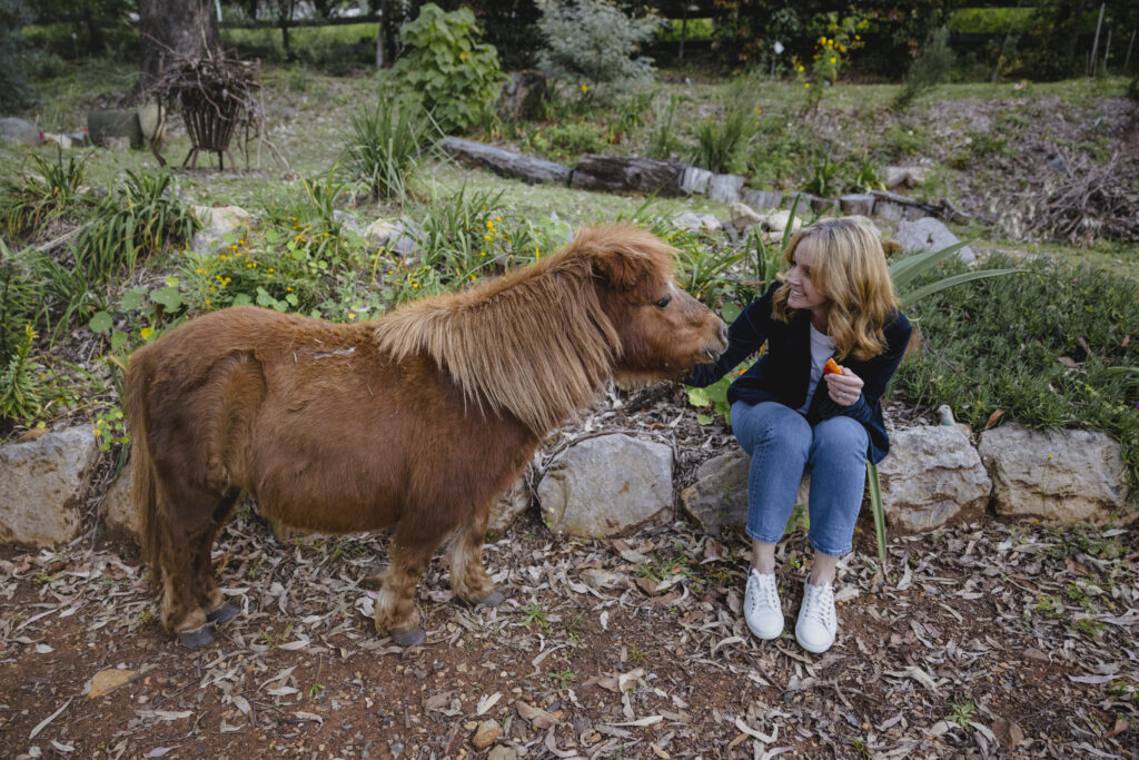 Katie excitedly feeds Gertie the miniature horse apple.
