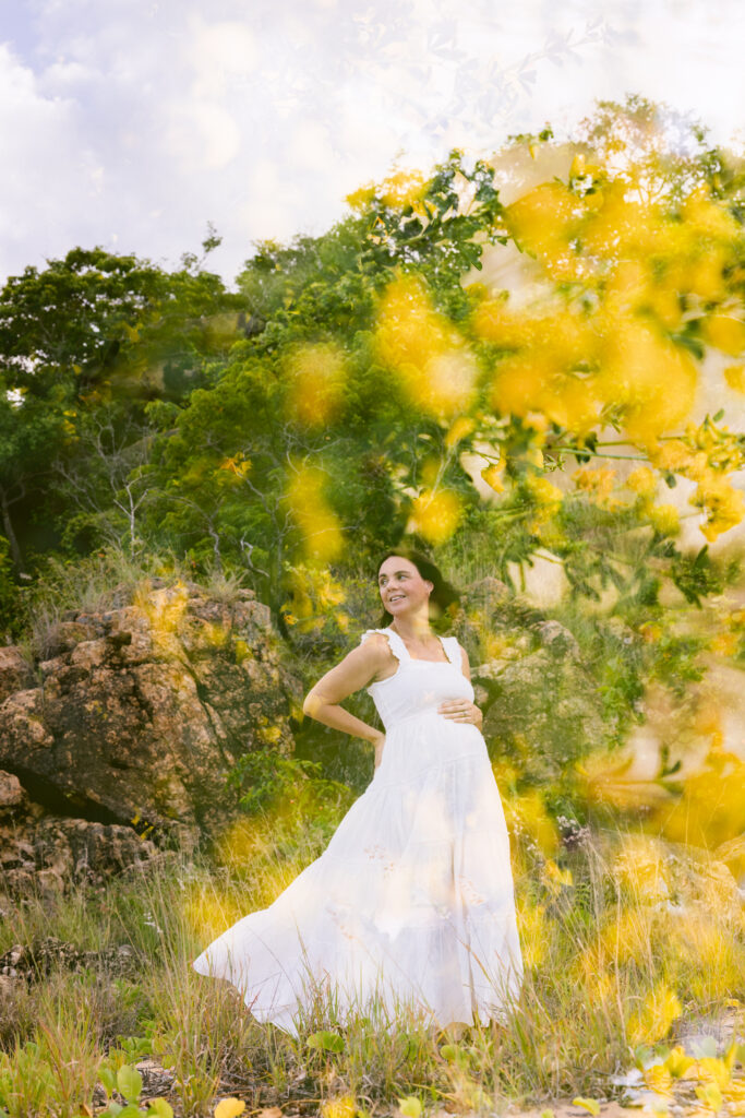 Double exposure images of a pregnant mum wearing a white dress standing looking back over her shoulder framed with yellow flowers.