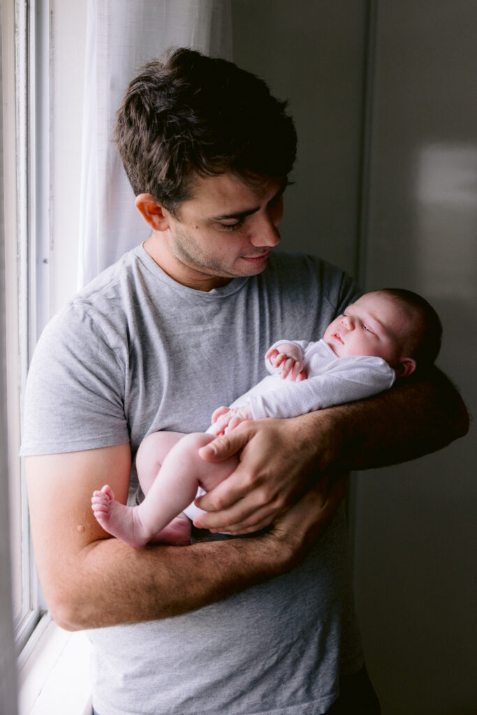 Dad looks lovingly at his newborn baby girl in his arms.