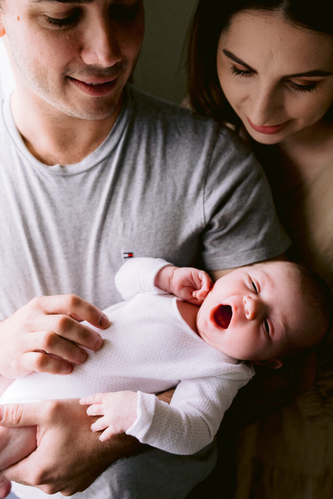 Photo of mum and dad holding their newborn daughter who is yawning in their home.