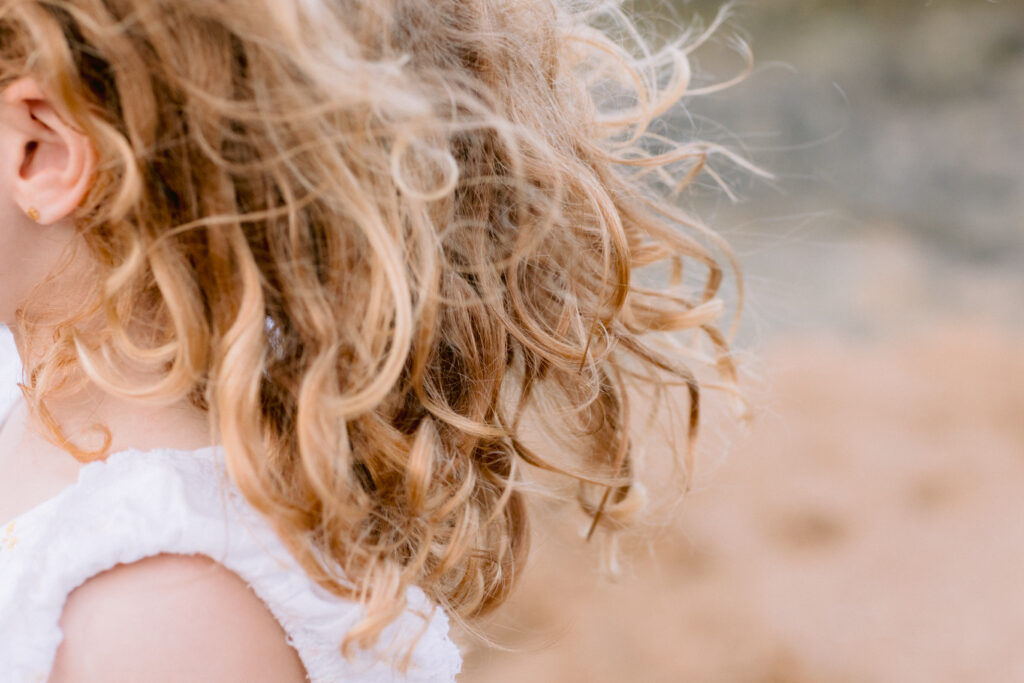 A daughters curly hair blows in the wind on the beach.