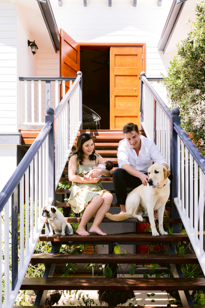 Family with newborn and dogs sit on their front steps.