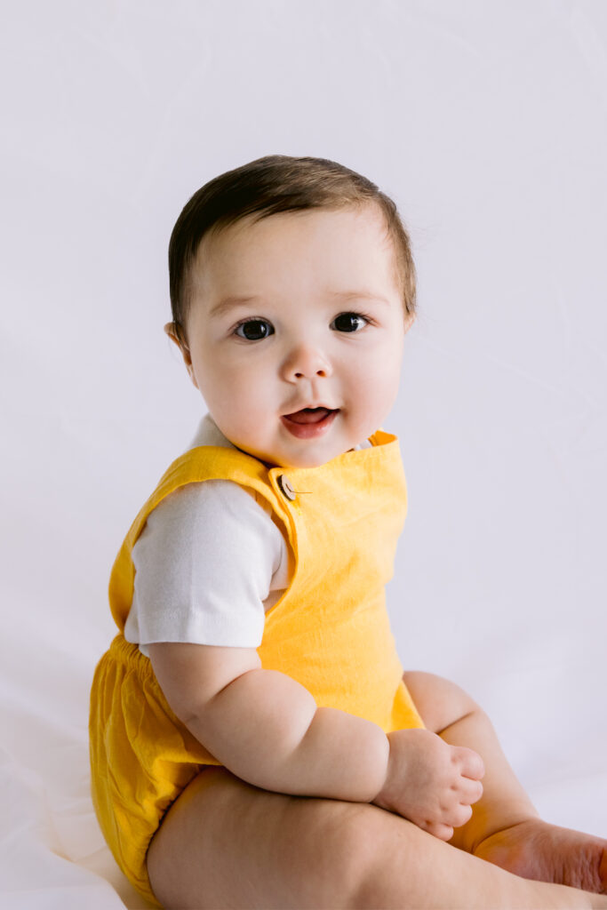 Headshot of baby boy smiling in a yellow romper