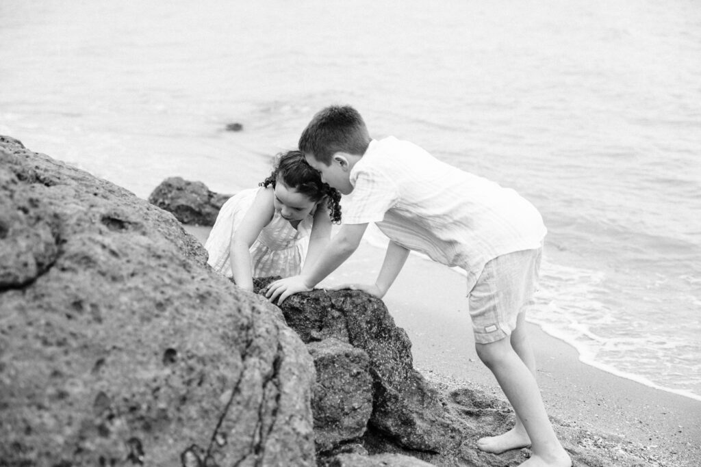A brother and sister explore the rocks on the beach together.