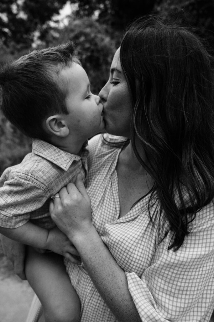 A black and white image of a little boy kissing his mother