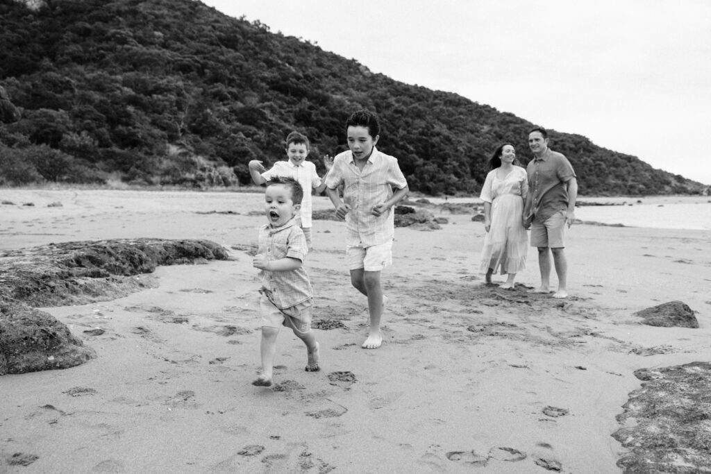 A family playing at the beach. The big brothers are chasing their younger brother.