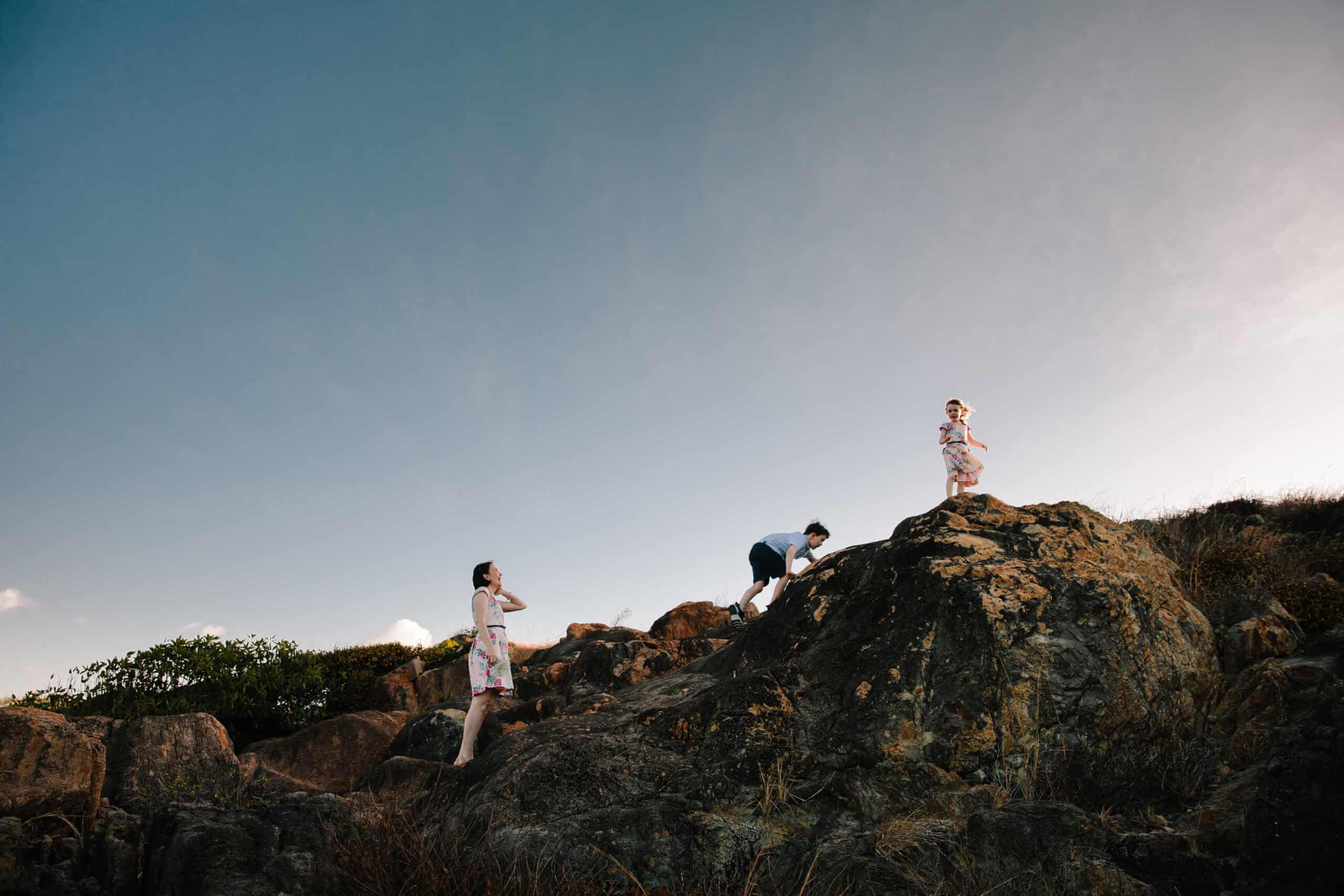 A mother watches her children climb over the rocks at at the beach