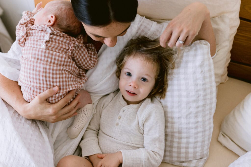 Mum is holding the baby girl and gently touching her sons hair