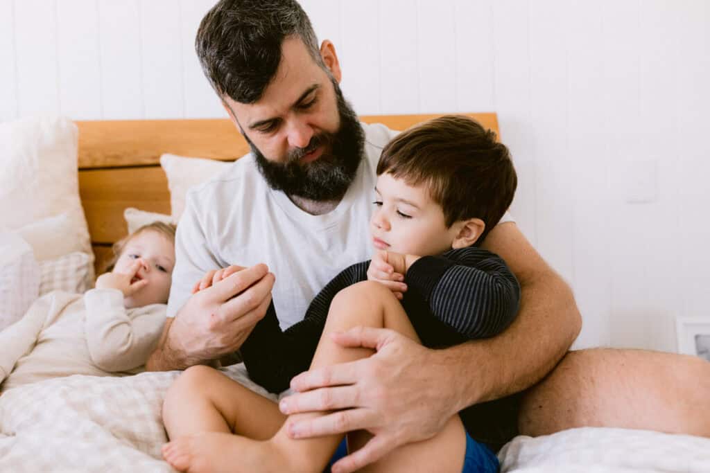 Dad is cuddling one son while the other son has his finger up his nose
