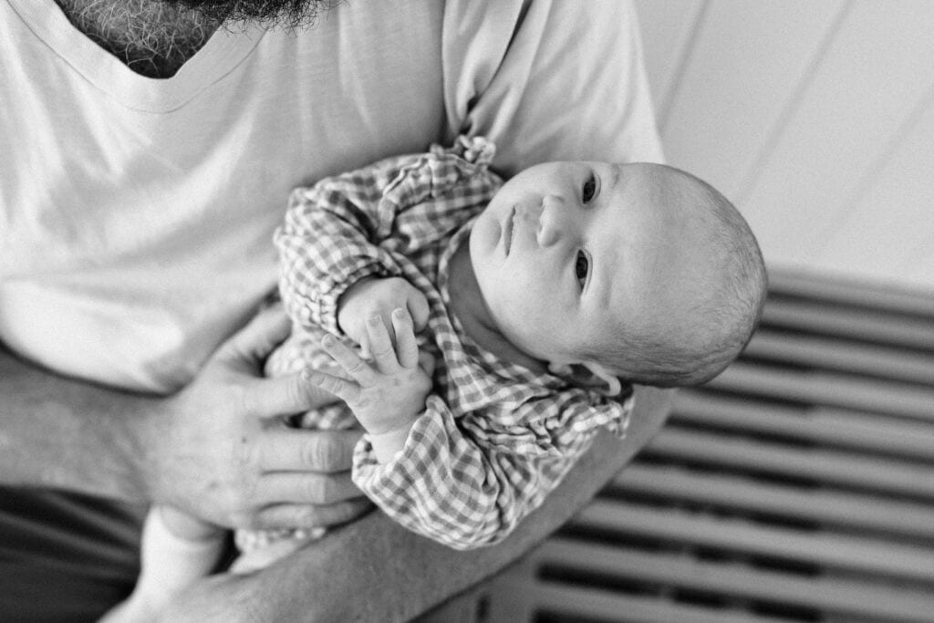 Baby girl is being held by her father and is looking up at him.