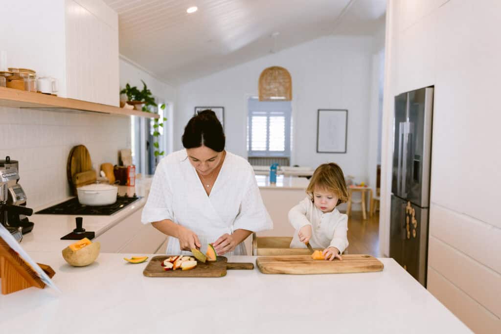 Mum and her young son are in the kitchen cutting up fruit.