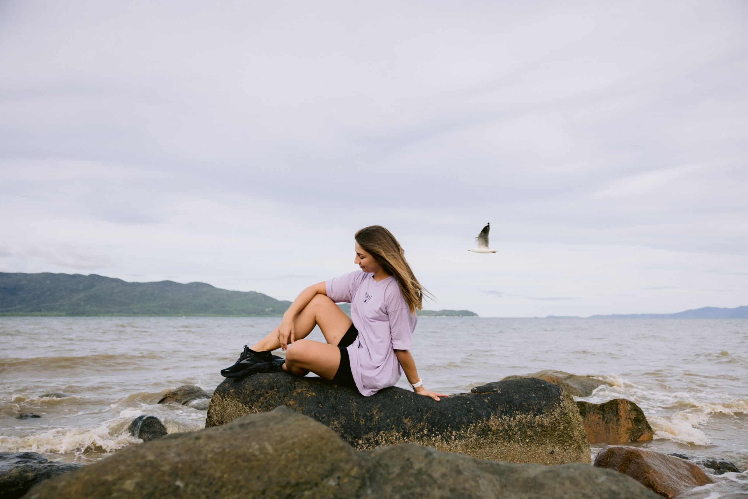 dance instructor sitting on a rock on the beach with a seagull flying by