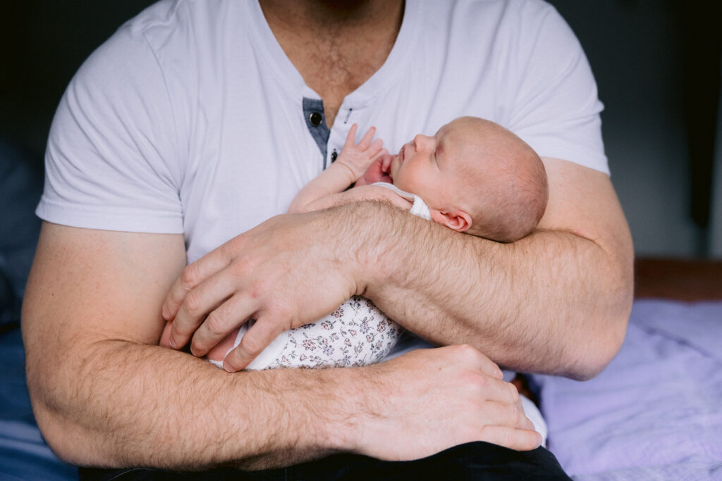 Dad holds the newborn baby girl in his big muscly arms
