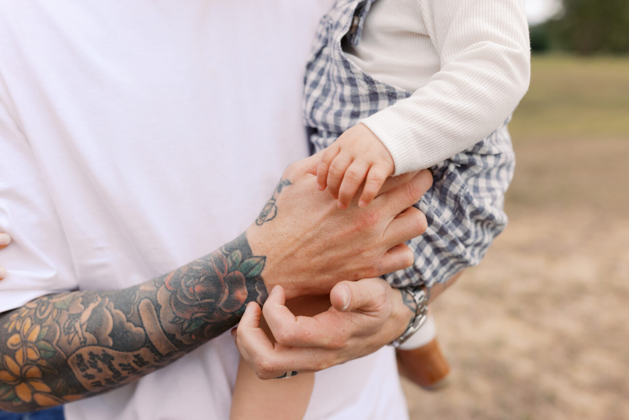 A close up photo of a father holding his little boy and their hands