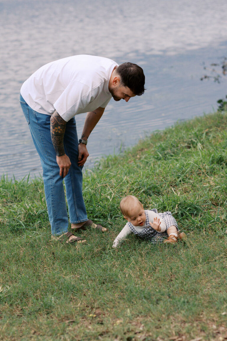 A father protects his son from reaching the water after his son has run off and then landed on the grass