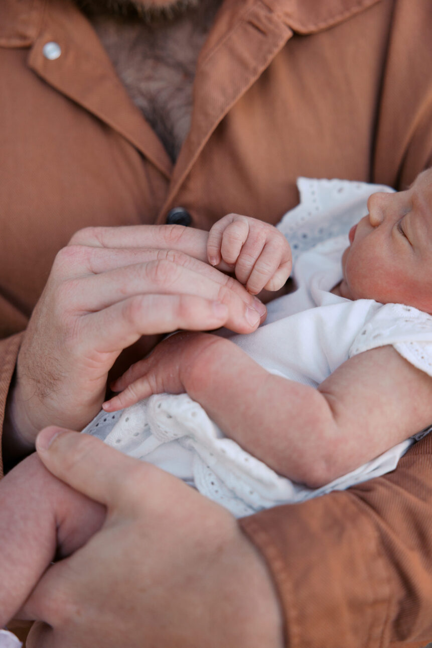 a father is holding his newborn and his big hands are on her little hands