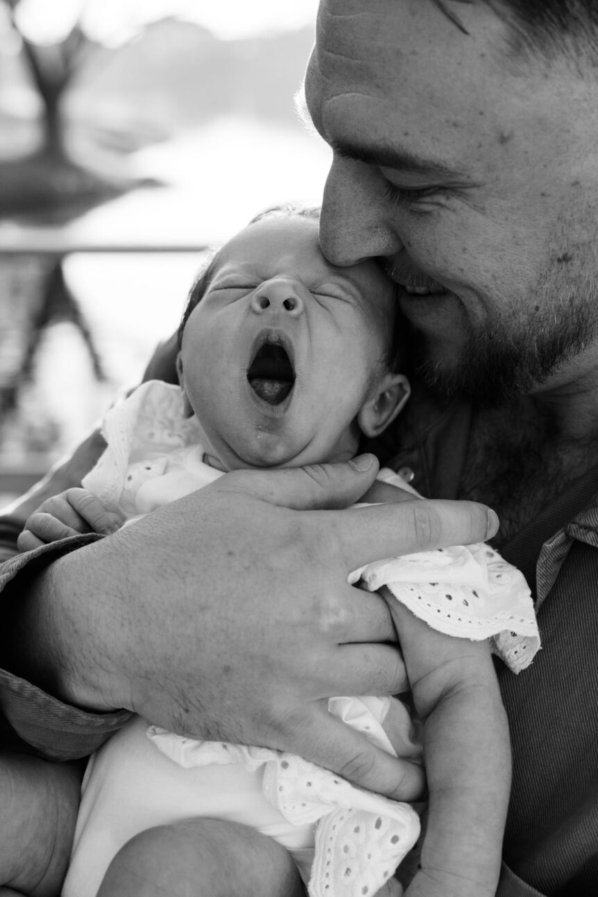 a father is holding his newborn and the baby is yawning