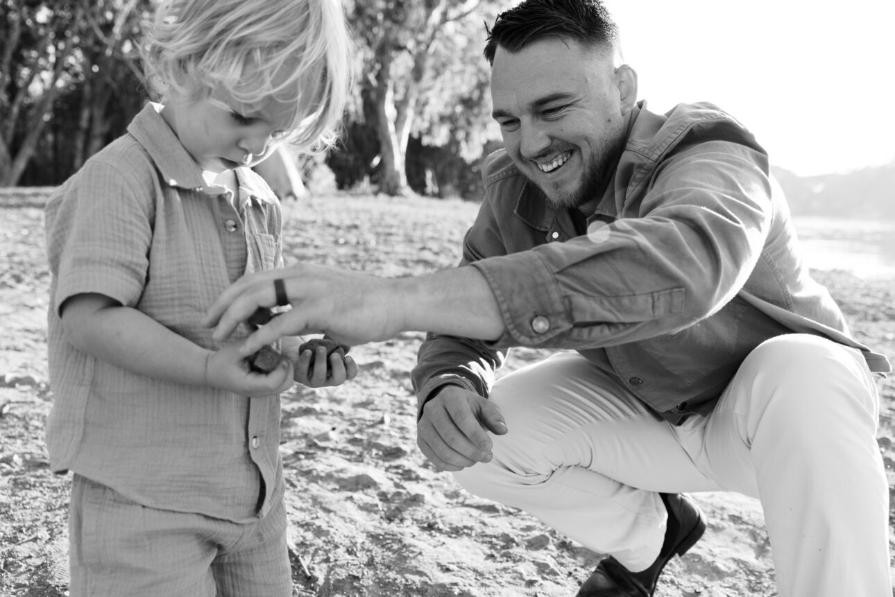 a father is collecting rocks for his son. The son is holding his hands full of the rocks
