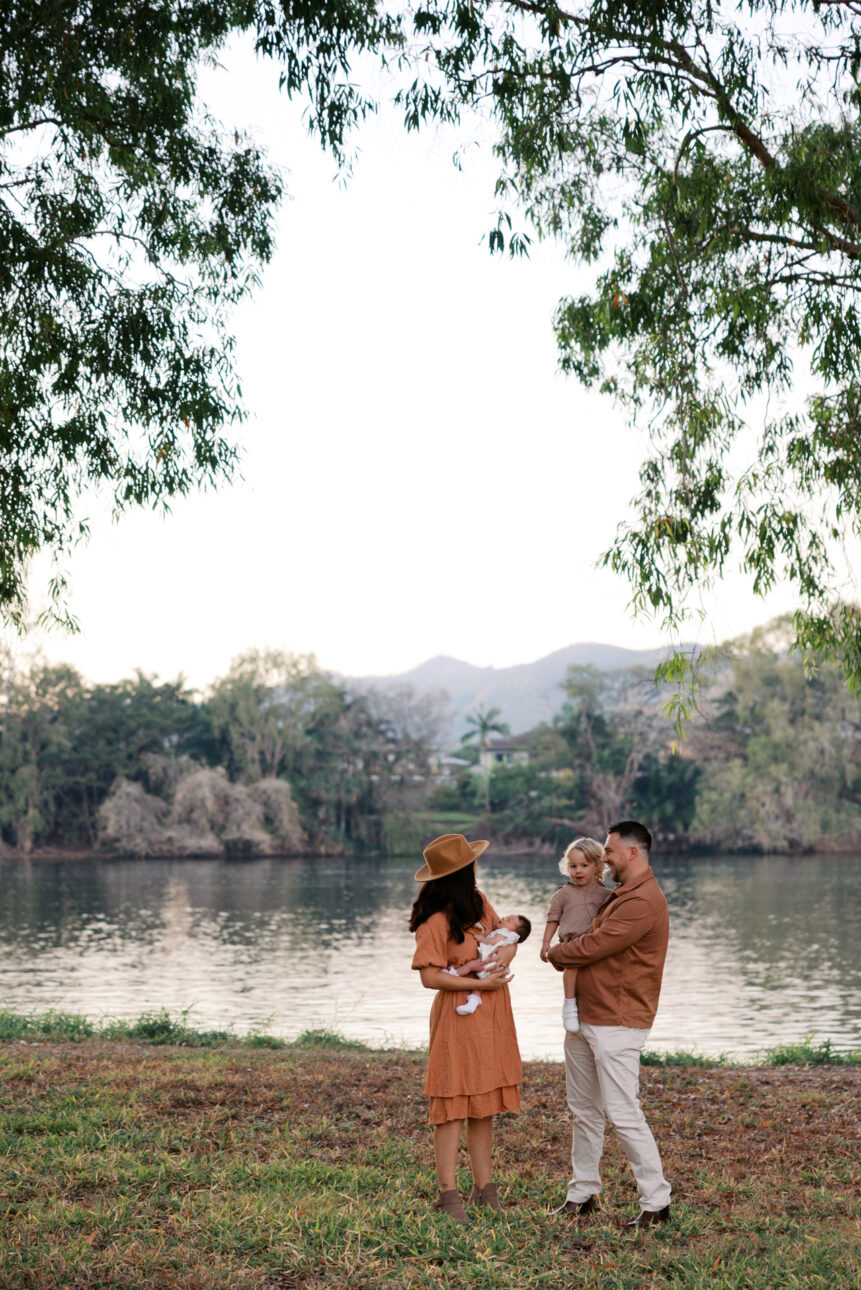 A mum holds her baby and the father holds the three year old down by a river early in the morning