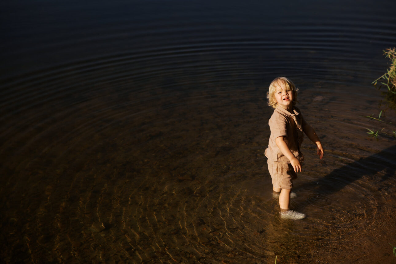 A three year old boy stands in the very shallow water of a creek bed