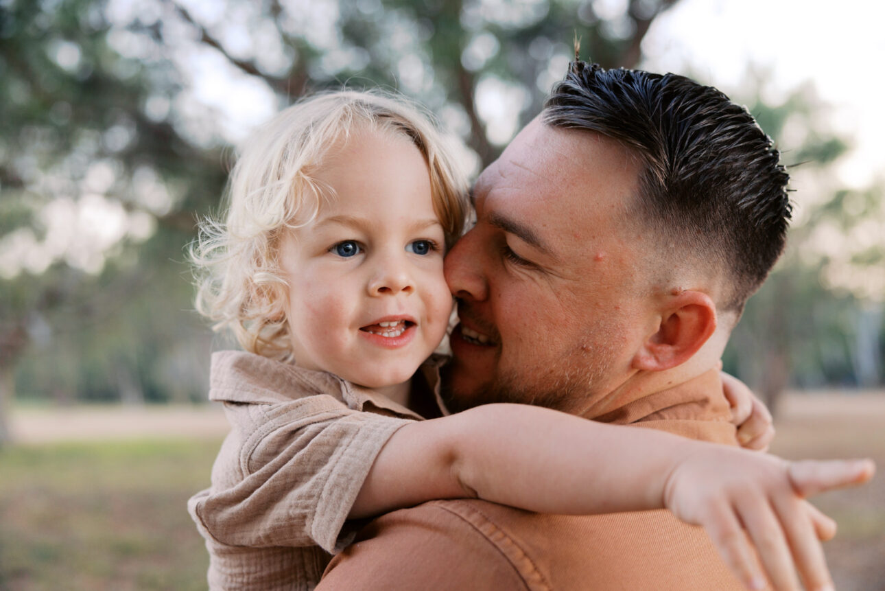 A father holds his little boy and the son has his arms around his neck