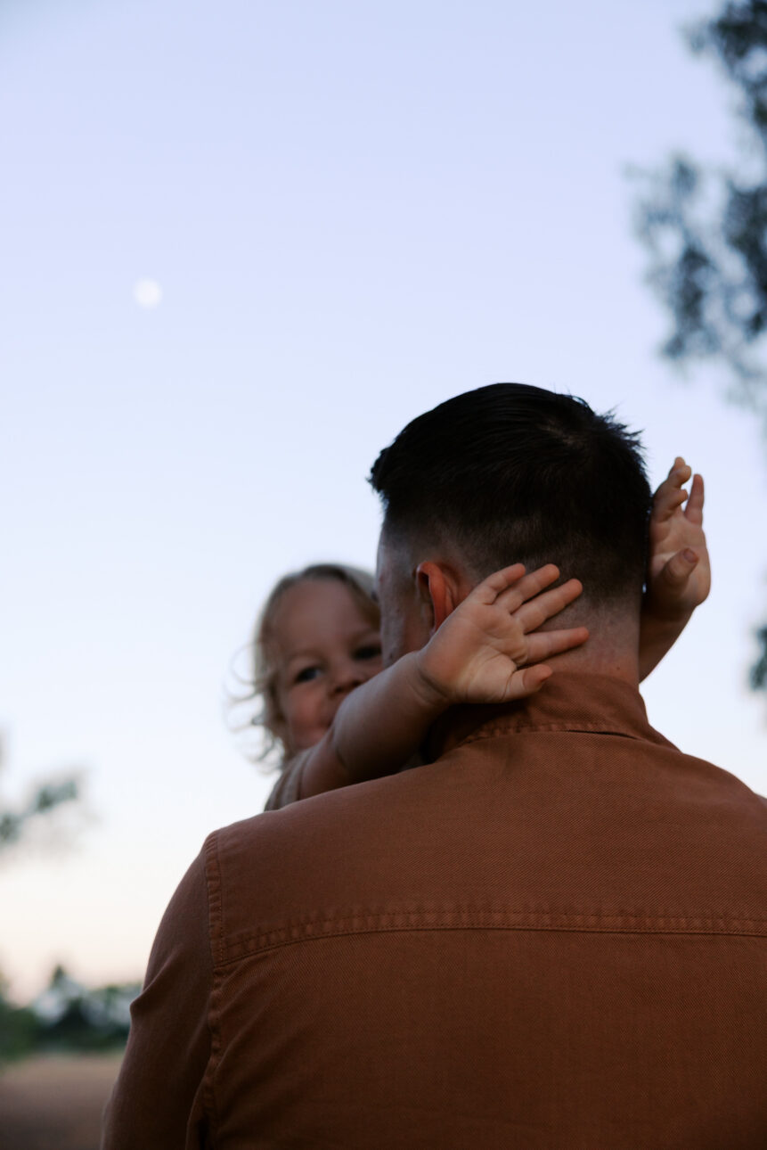 A father holds his son at sunrise the moon is still seen in the sky