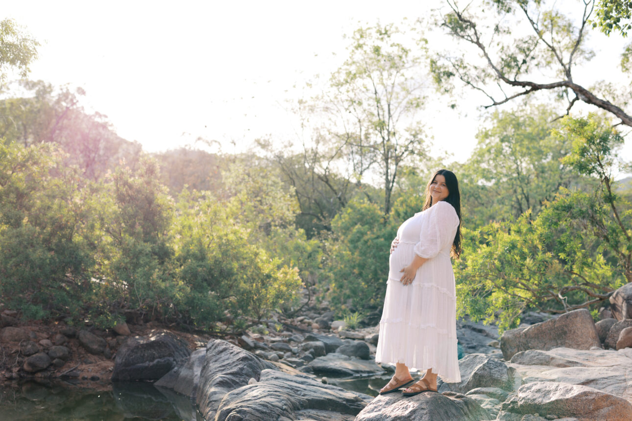 Maternity Photo of a Pregnant lady in a white dress standing in a dry creek bed