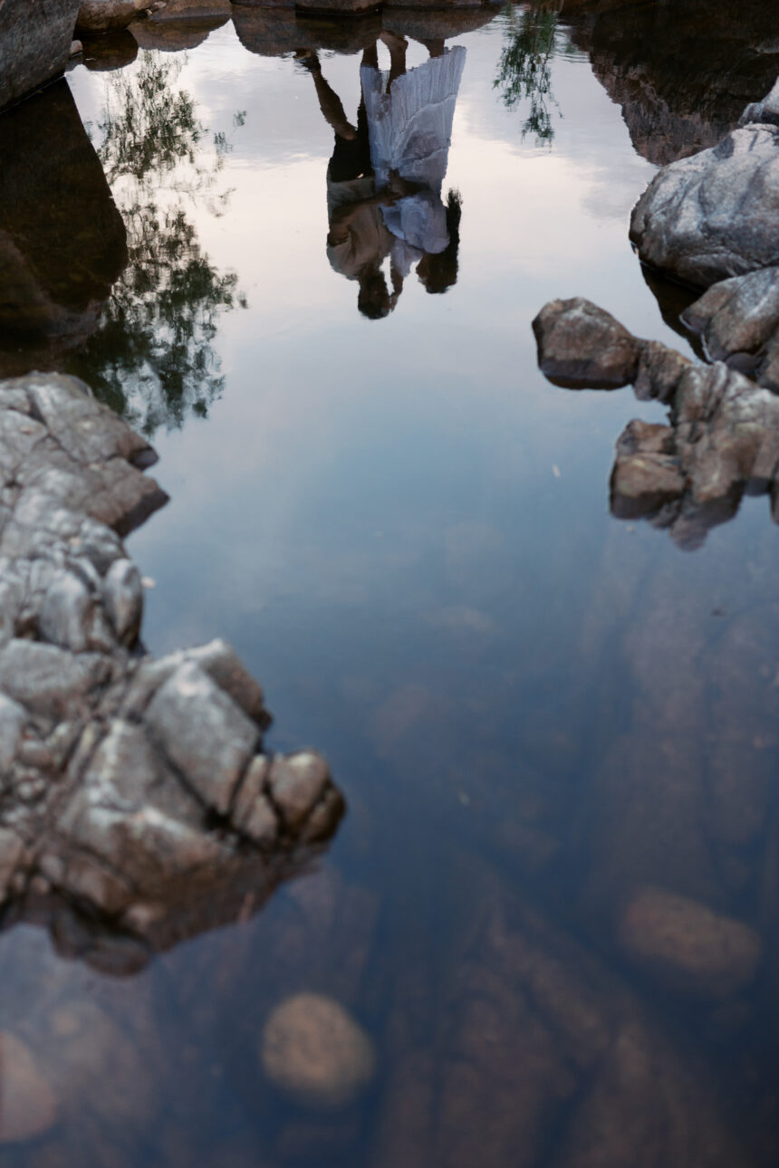 a reflection of a husband and wife in the creek. The boarder of the image has rocks around it