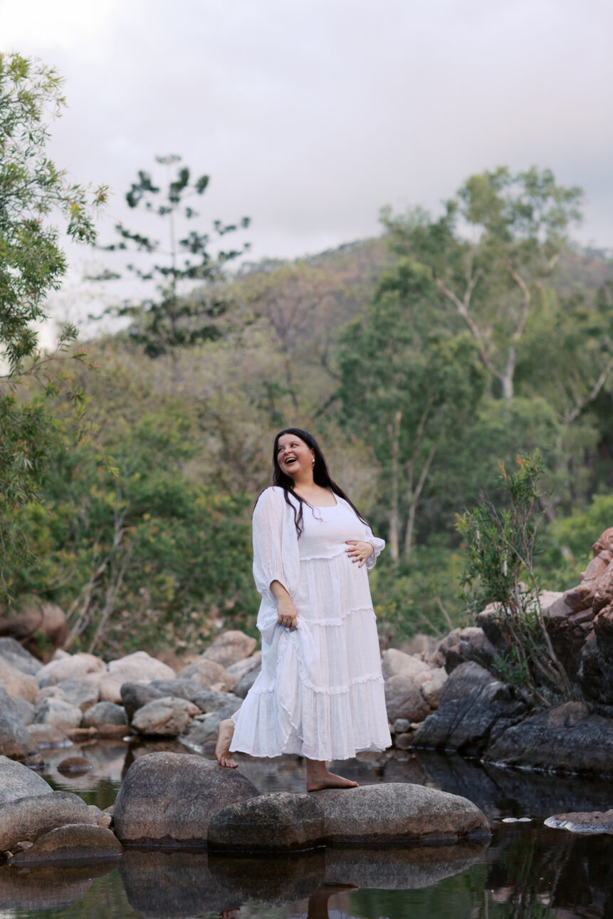 Maternity Photo of a Pregnant lady in a white dress standing on a rock in the middle of a creek