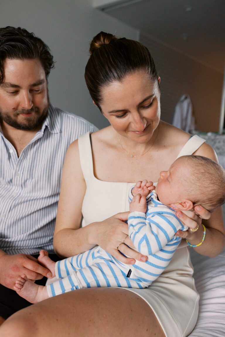 Mum and Dad sit on a bed in the hotel at Ardo holding their new baby