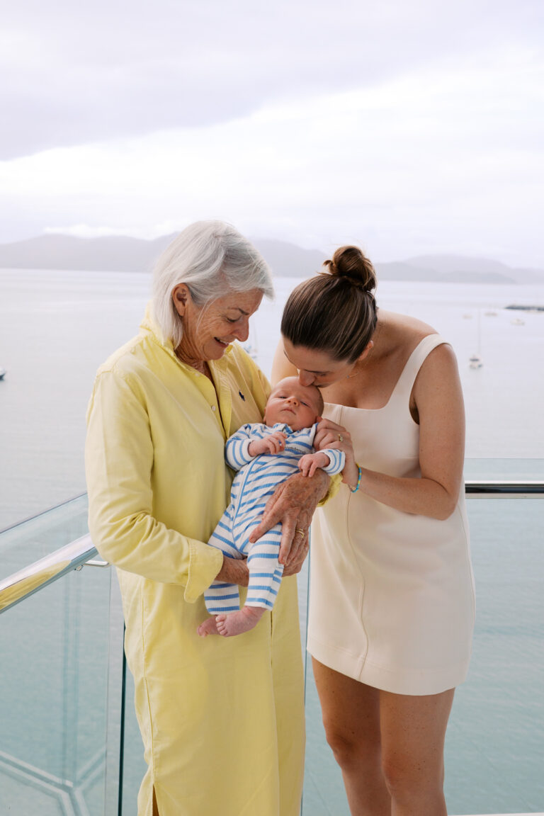 A grandmother is holding her baby grandson and her daughter his kissing her baby
