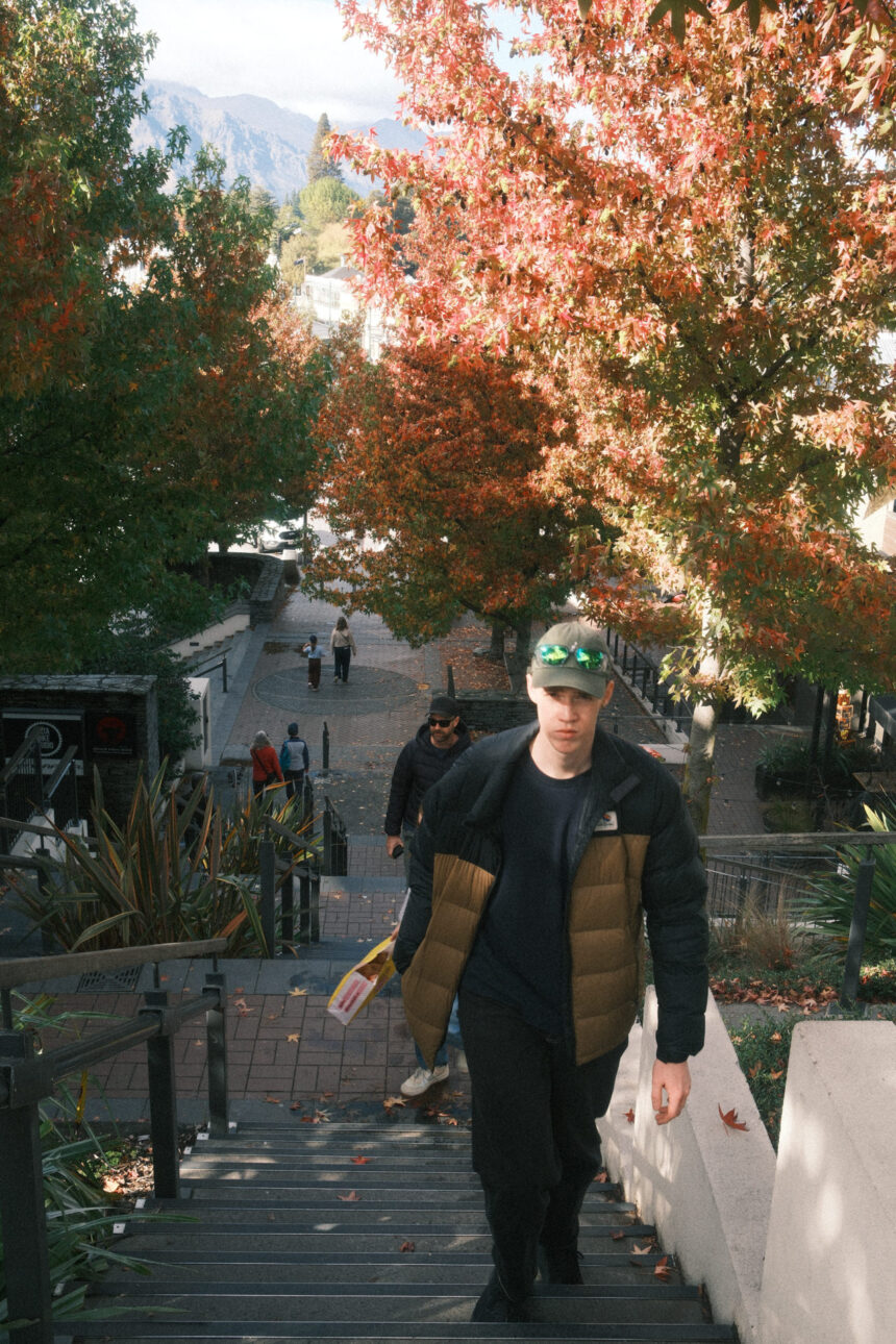 a young man is walking up the stairs in Queenstown with Autumn leaves in the background