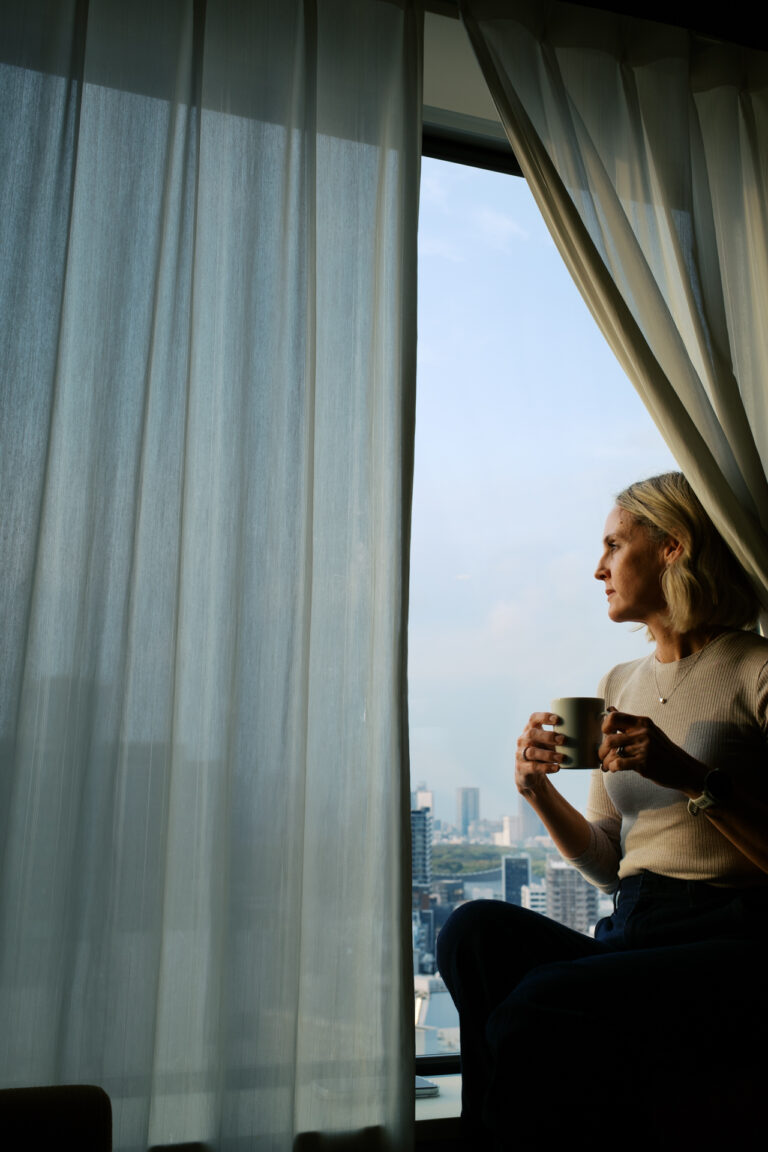 Katie is sitting on the window ledge inside the room looking out over Shibuya crossing