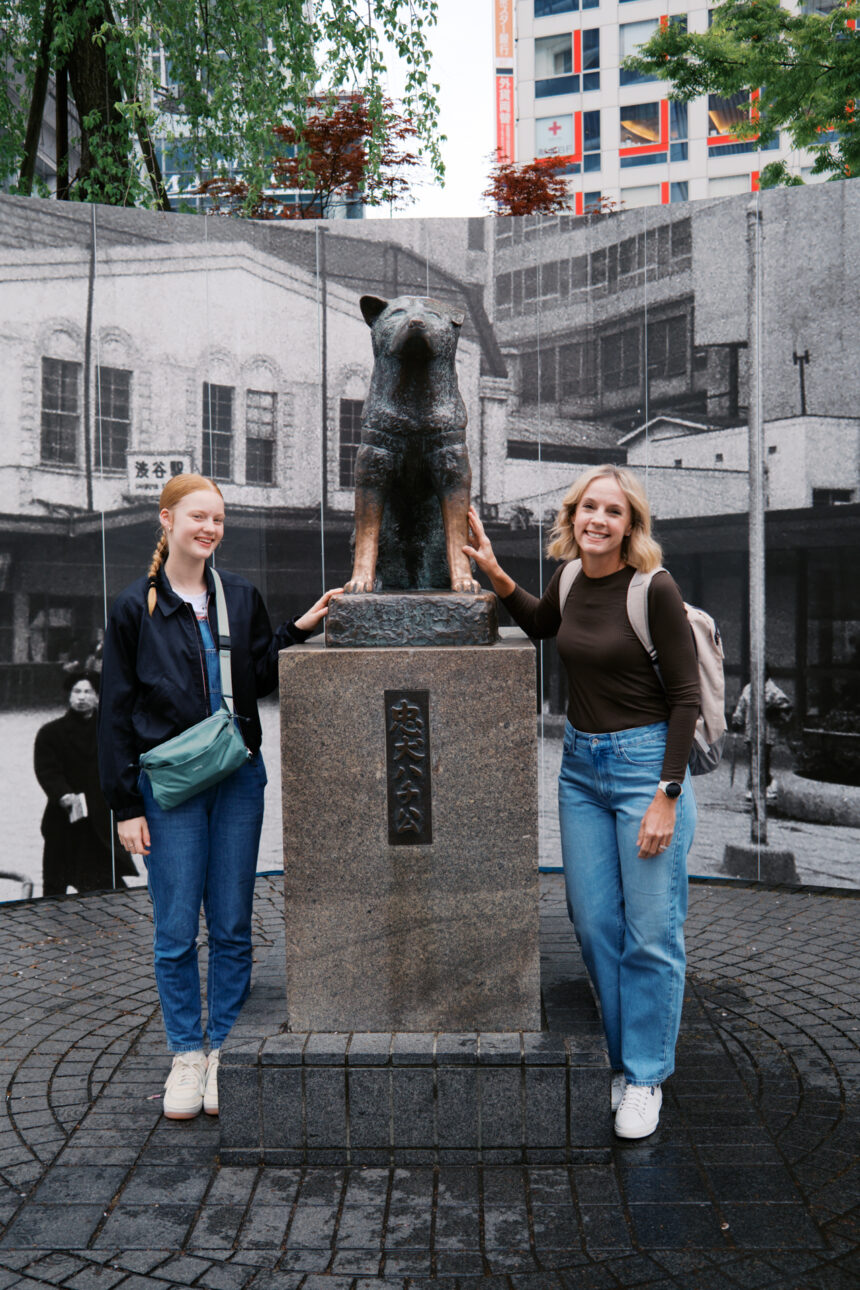 Katie and Frankie are standing next to the statue of Hauchi the dog in Shibuya