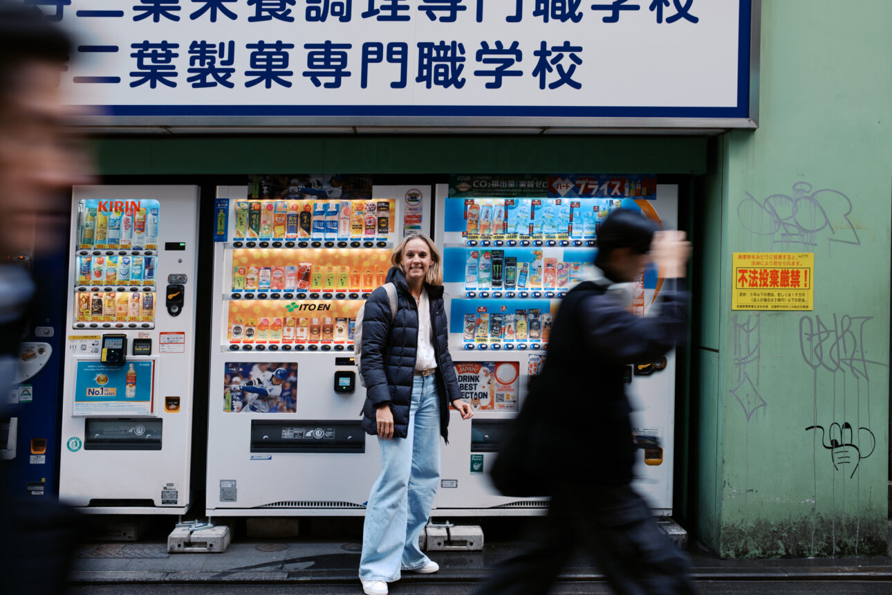 Katie is standing in front of vending machines in Tokyo