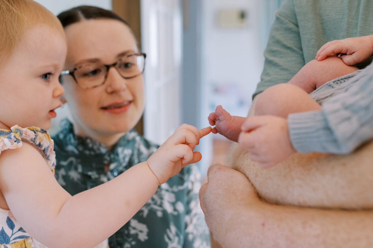 A little sister gently touches her newborn brothers toes