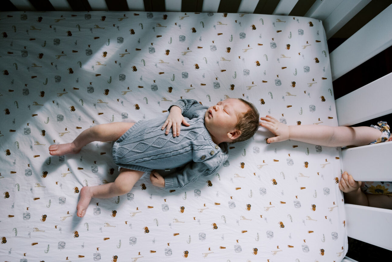 a little sister puts her hand through the cot and gently touches her baby brothers head