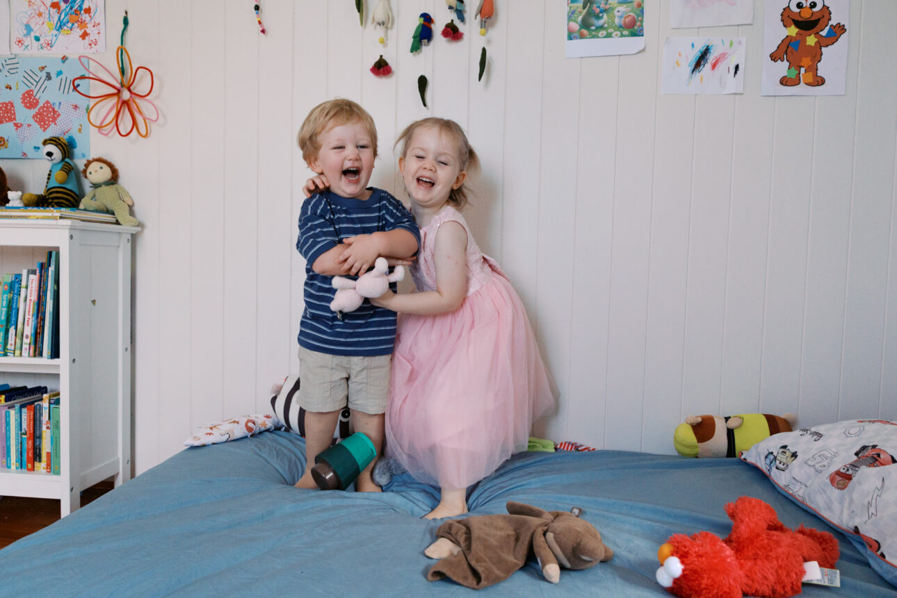 a young brother and sister close in age are laughing and hugging each other.